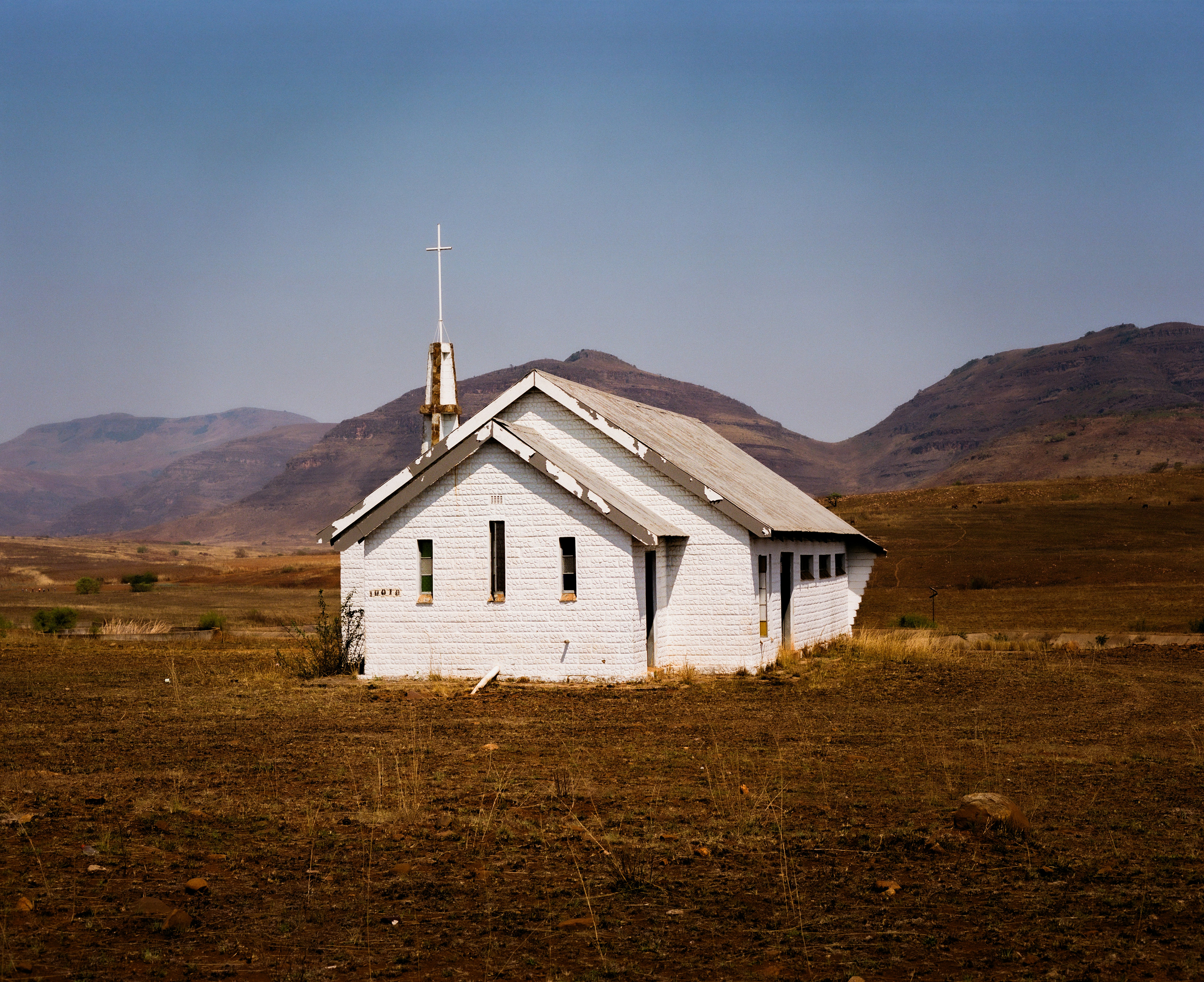 A small white church in a field with mountains in the background