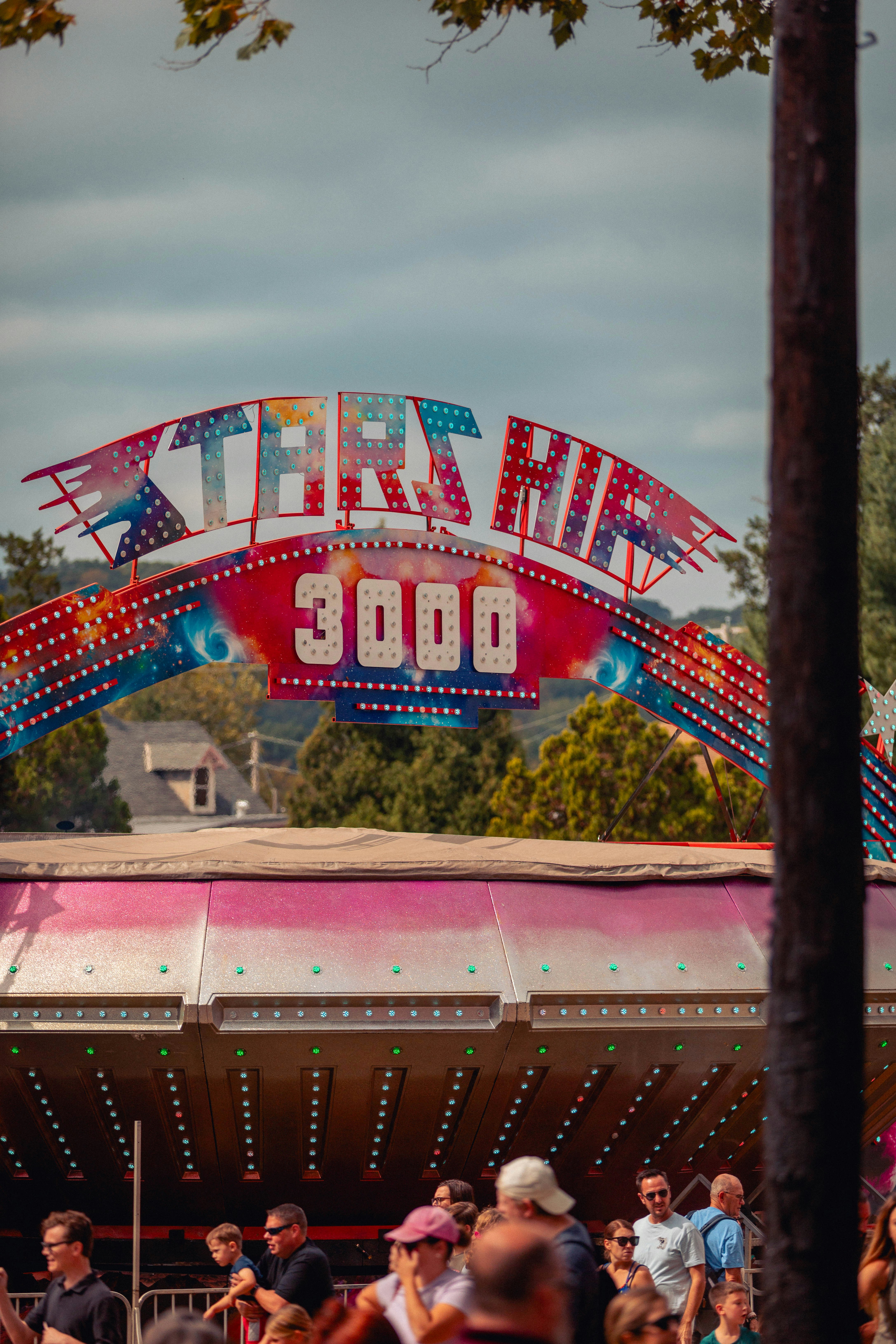 Kerumunan orang berdiri di sekitar wahana karnaval