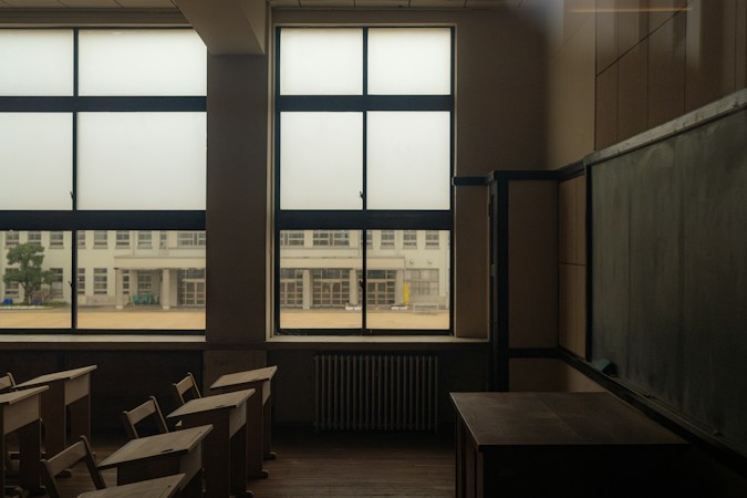 A quiet classroom with wooden desks, tall windows and a chalkboard, the kind of space school funding decisions shape every year