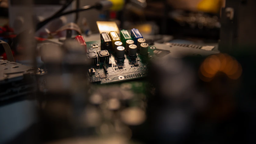 A close-up of a circuit board on a workbench under low light.