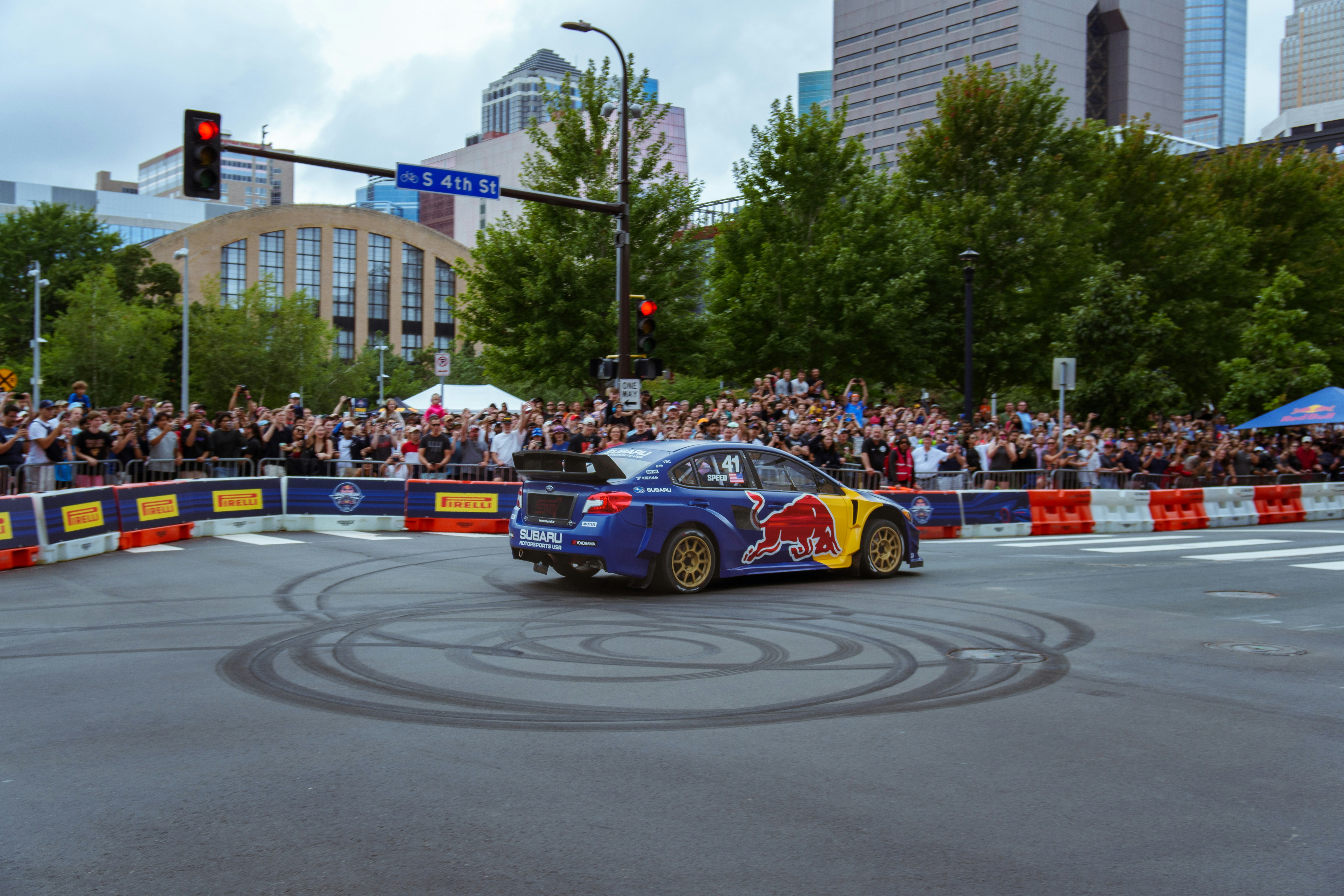 A blue car driving down a street next to a crowd of people
