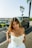 A woman in a white dress standing in front of a car