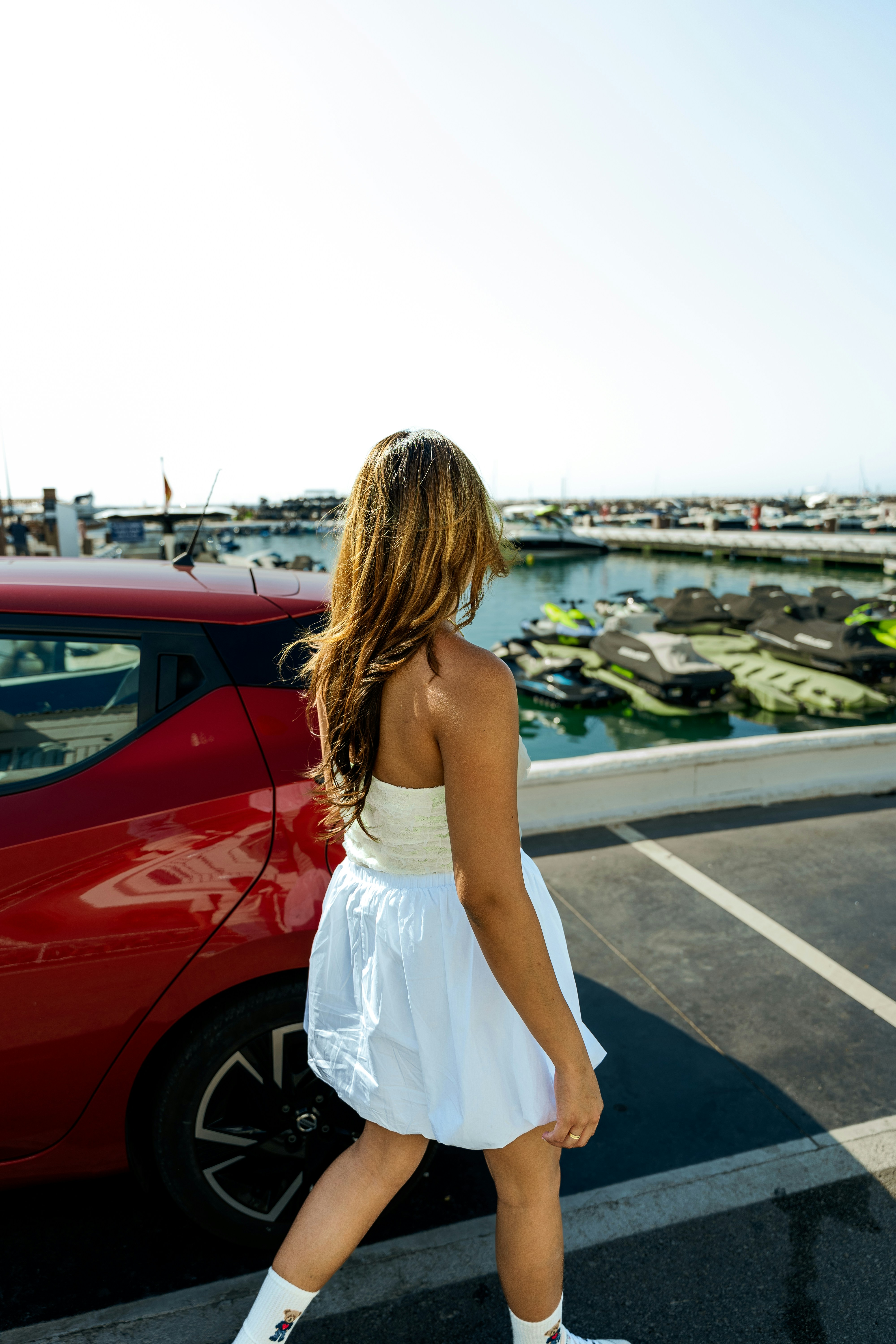 A woman walking across a parking lot next to a red car