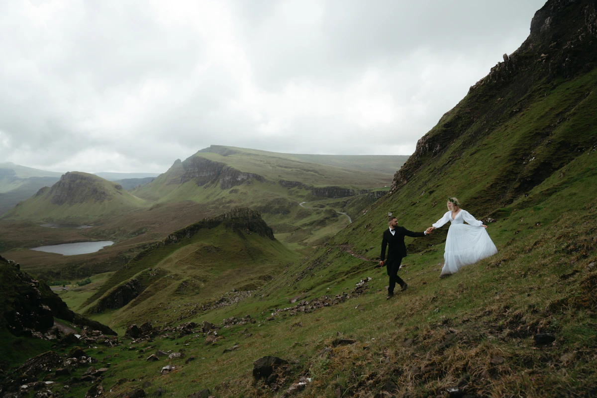 A bride and groom holding hands while walking up a grassy hillside during their elopement