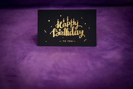 A black and gold happy birthday card on a purple background