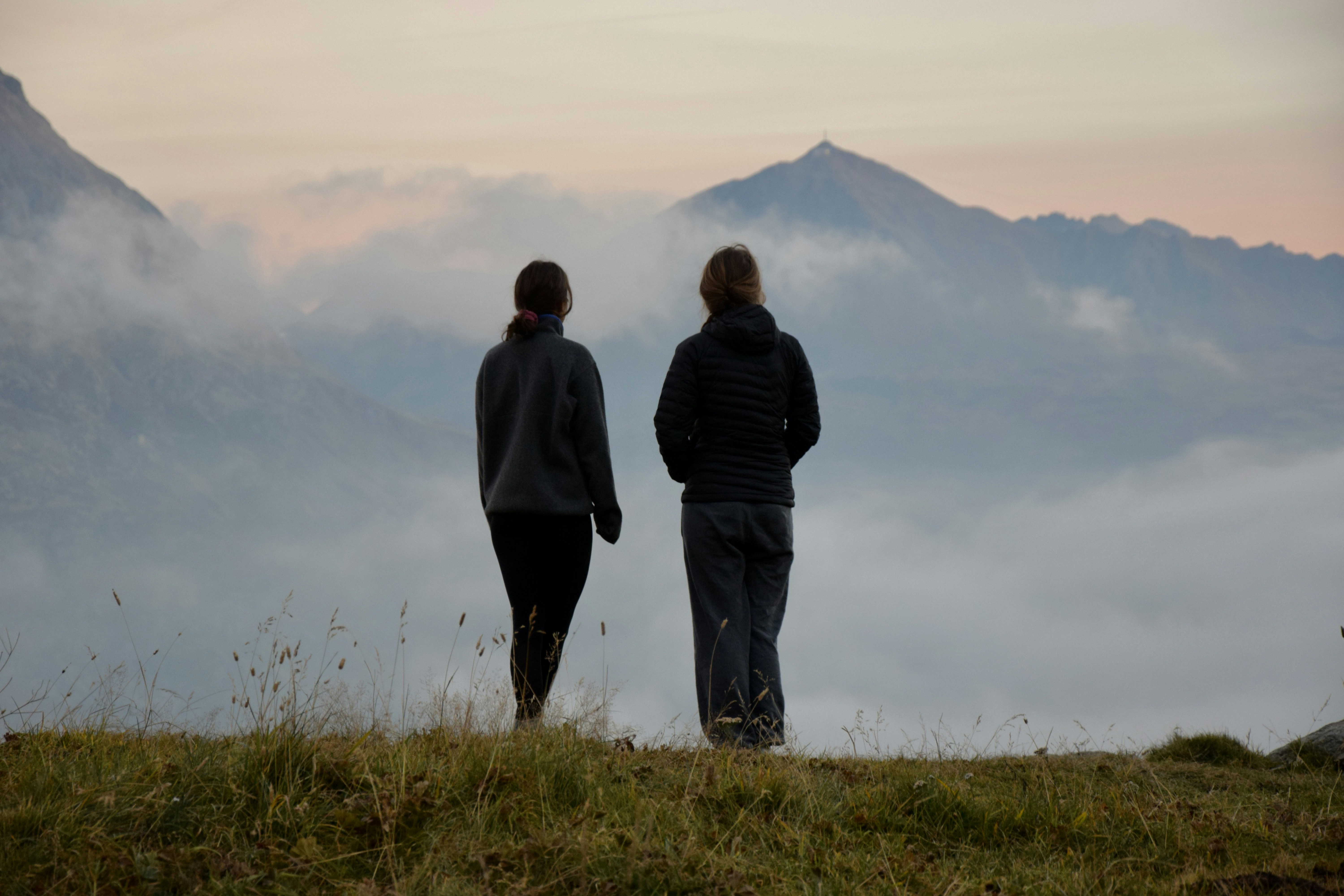 A couple of people standing on top of a grass covered hill