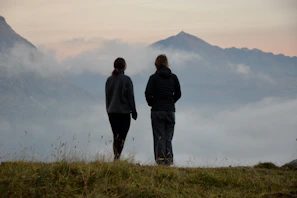 A couple of people standing on top of a grass covered hill