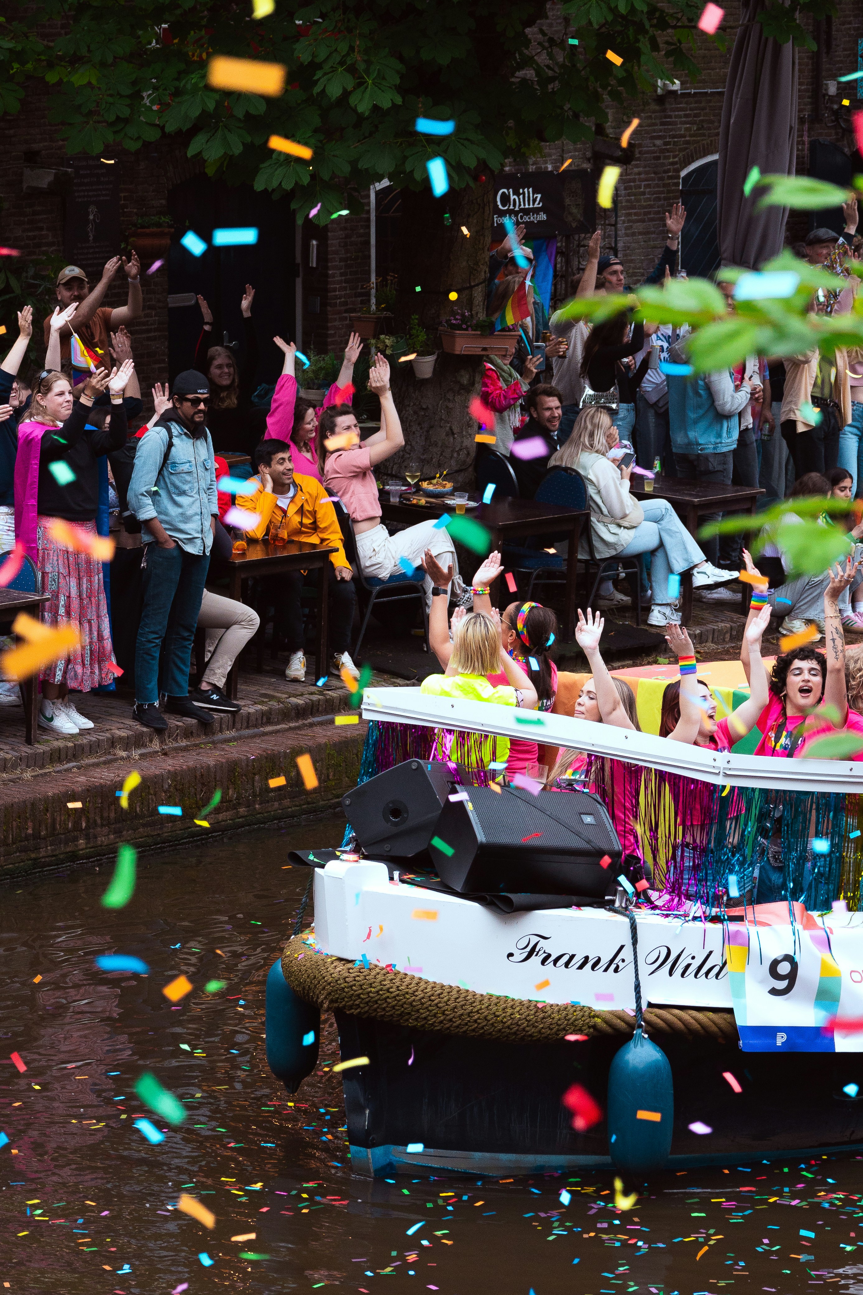Gente celebra en un barco decorado y orilla de canal con confeti.