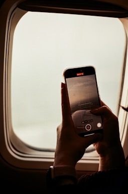A person holding a cell phone in front of an airplane window