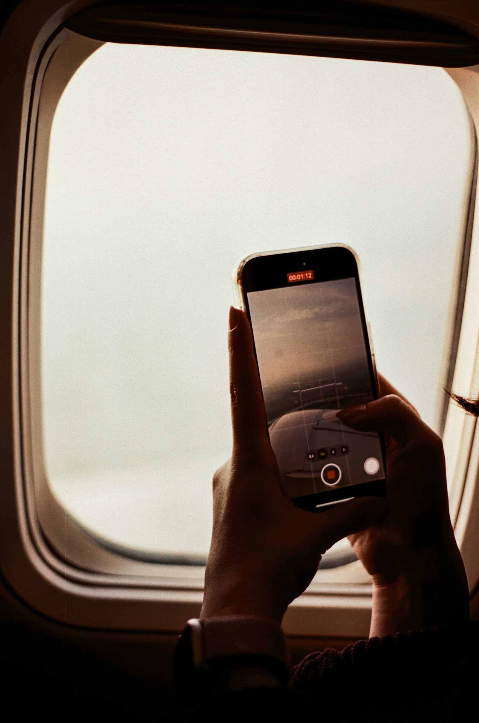 A passenger holding a phone beside an airplane window above the clouds
