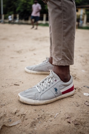 A person standing on a dirt road wearing white shoes