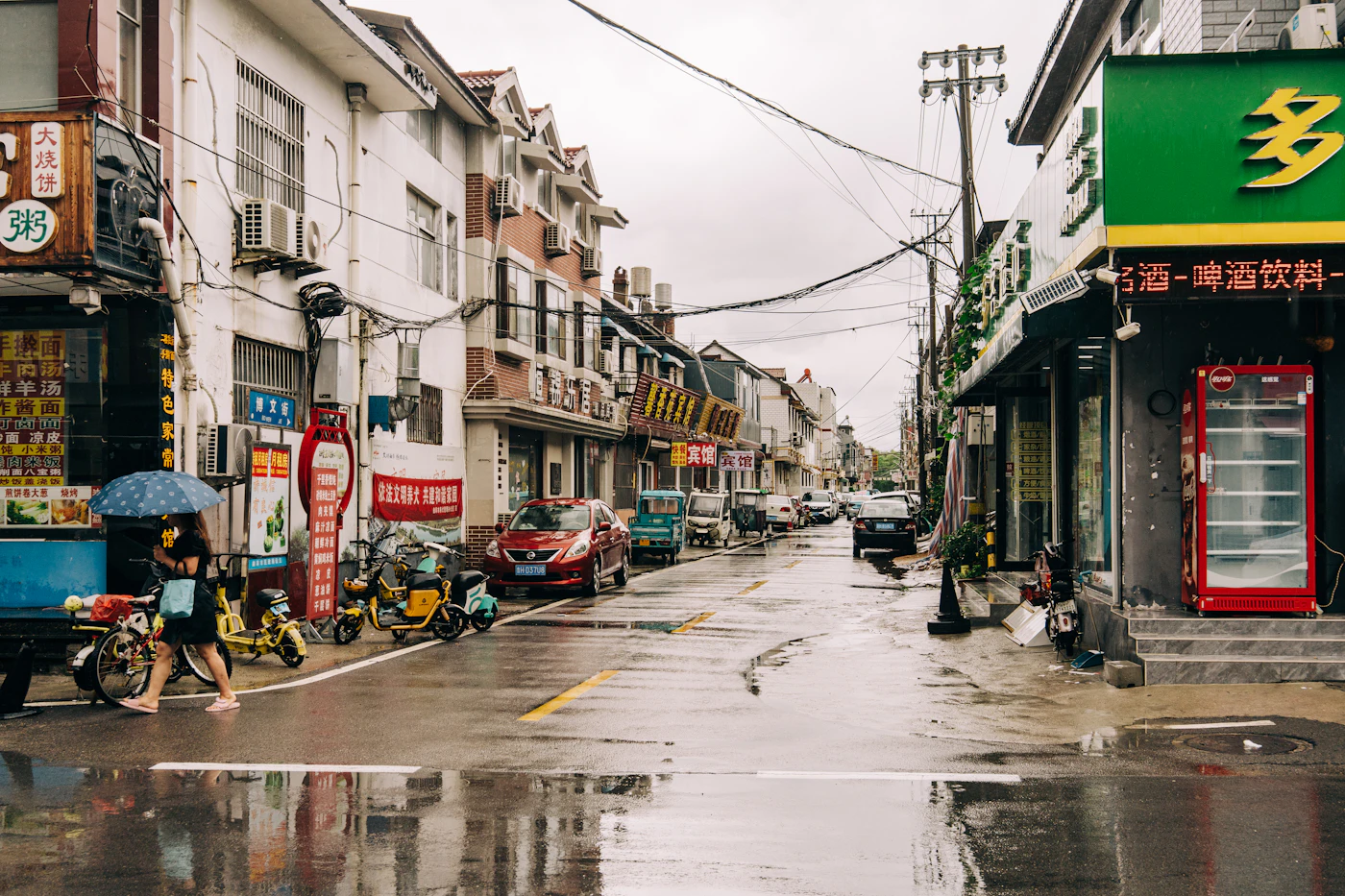 A pedestrian with a blue umbrella crossing a rainy street