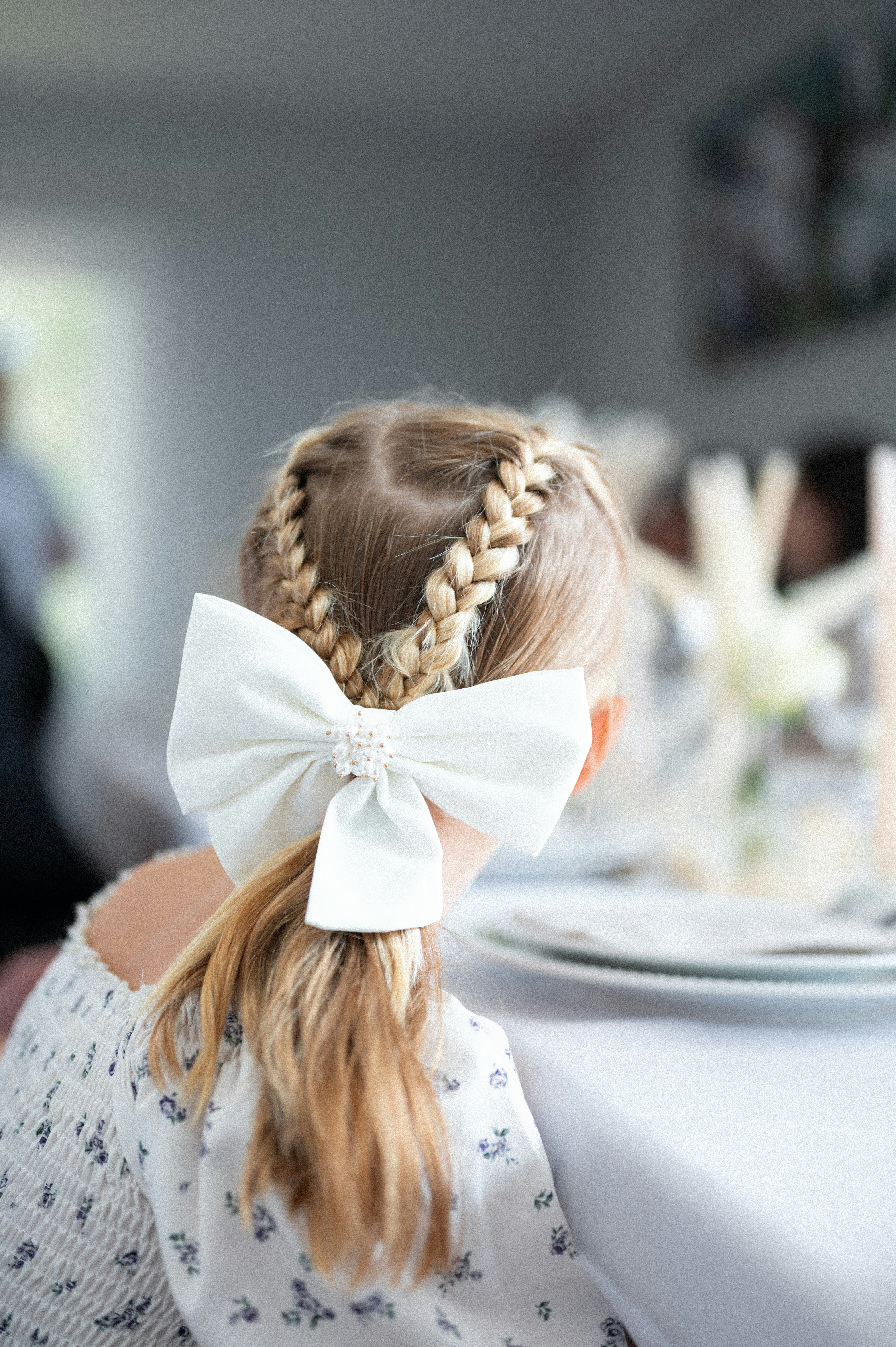 A little girl sitting at a table with a white bow in her hair