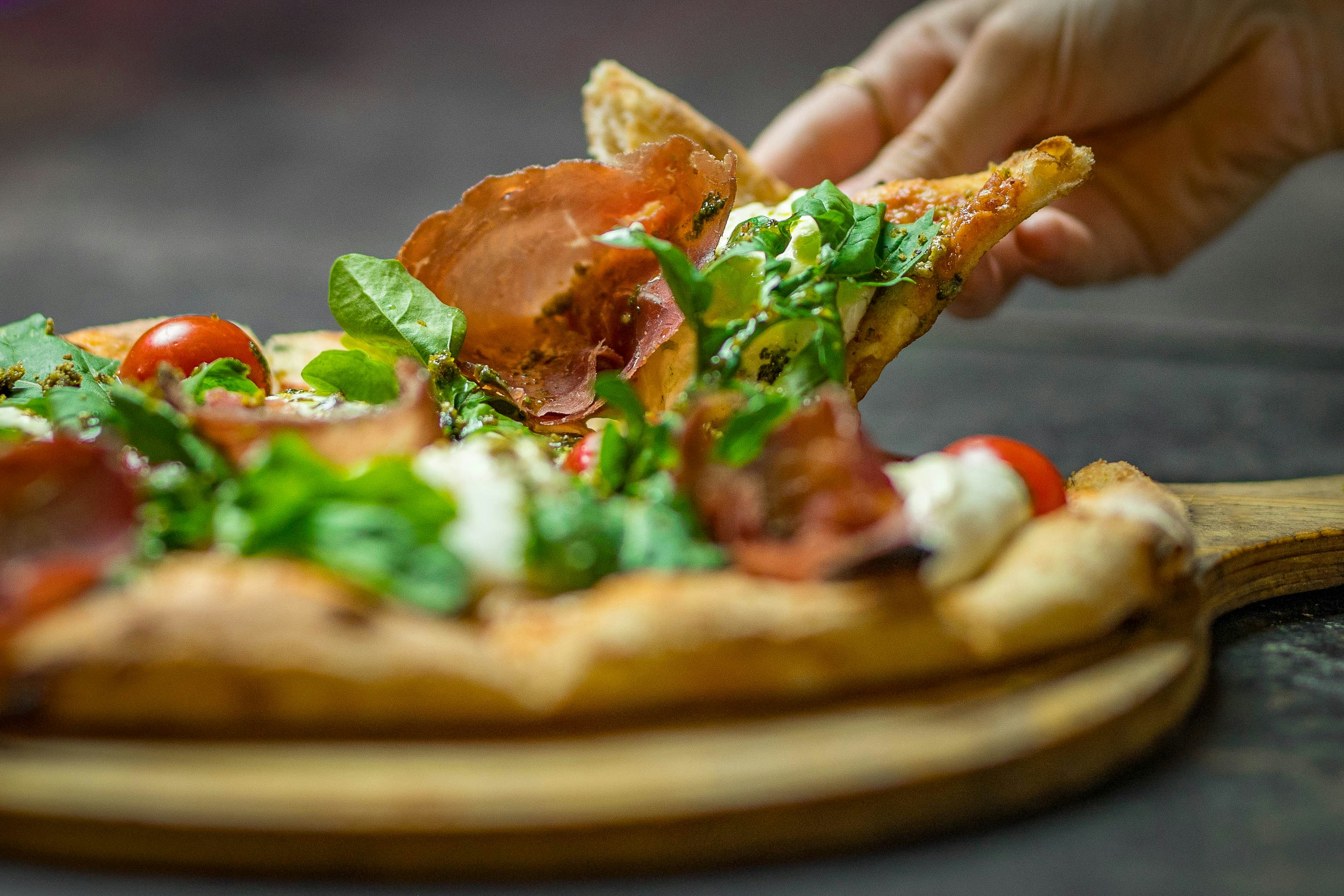 Una persona tomando un trozo de pizza de un plato de madera
