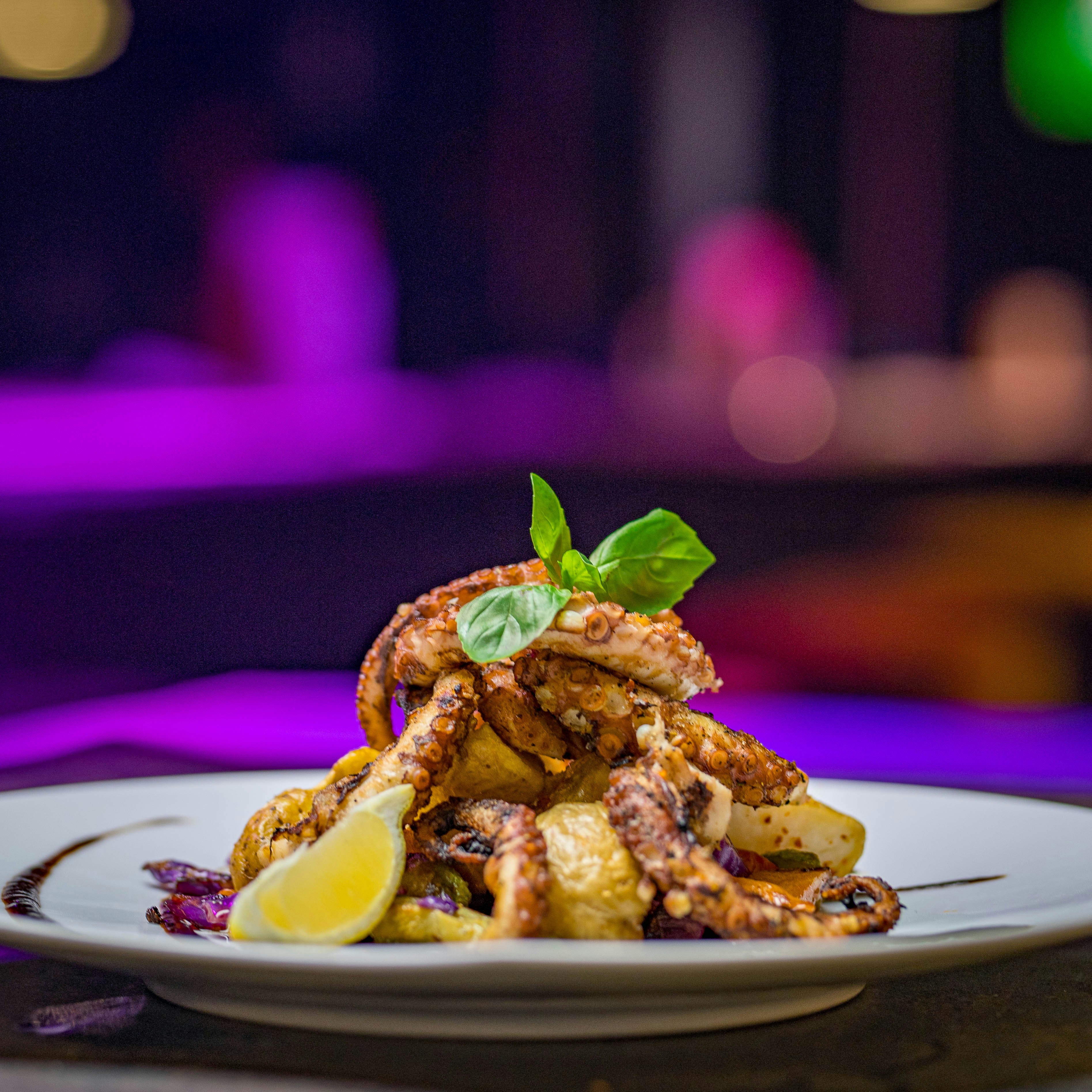 Pulpo a la brasa sobre puré de patata en plato de cerámica blanca, iluminación suave de restaurante íntimo