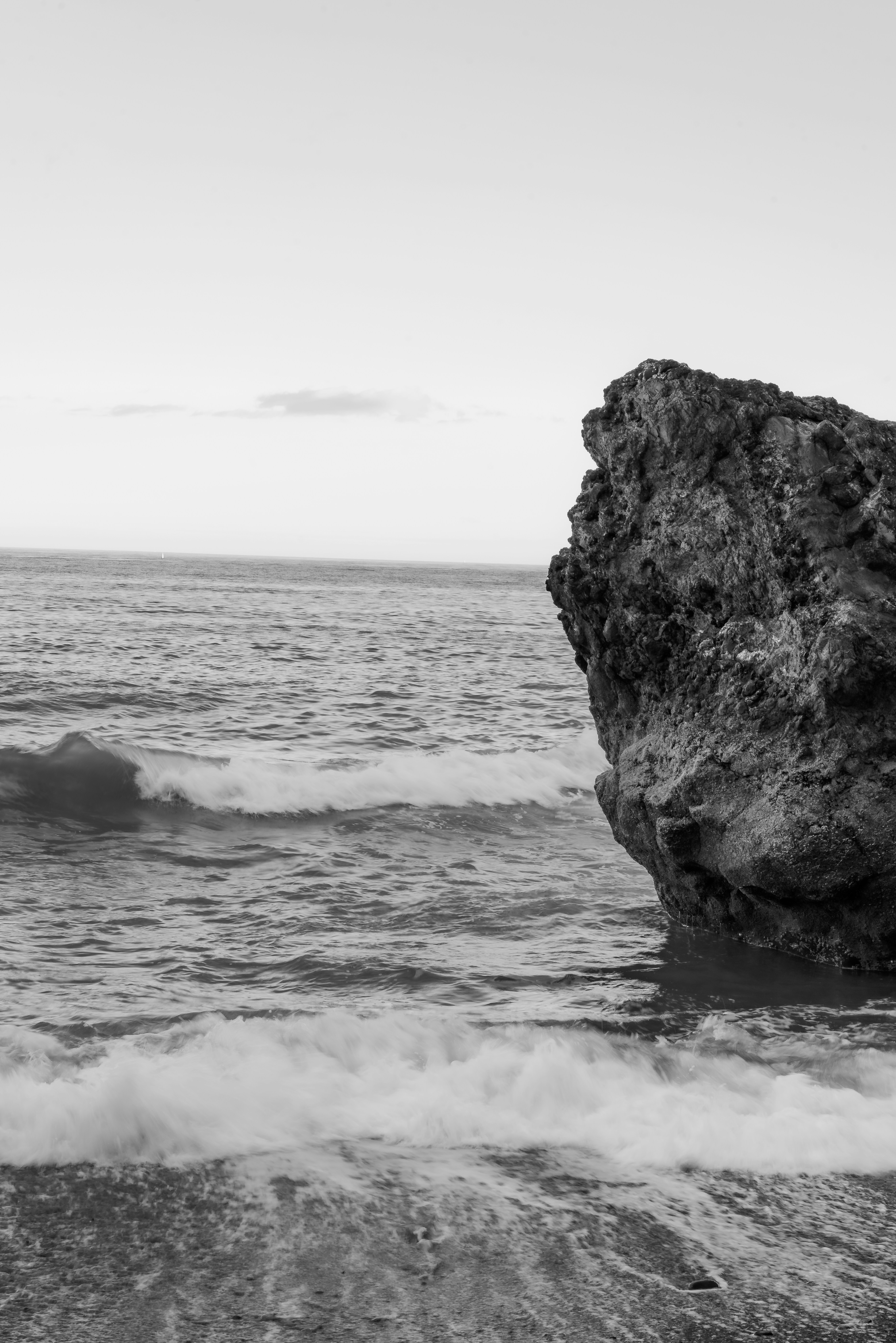 A black and white photo of the ocean with a rock sticking out of the water