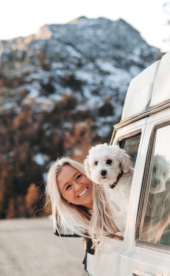 A woman holding a white dog in the back of a van