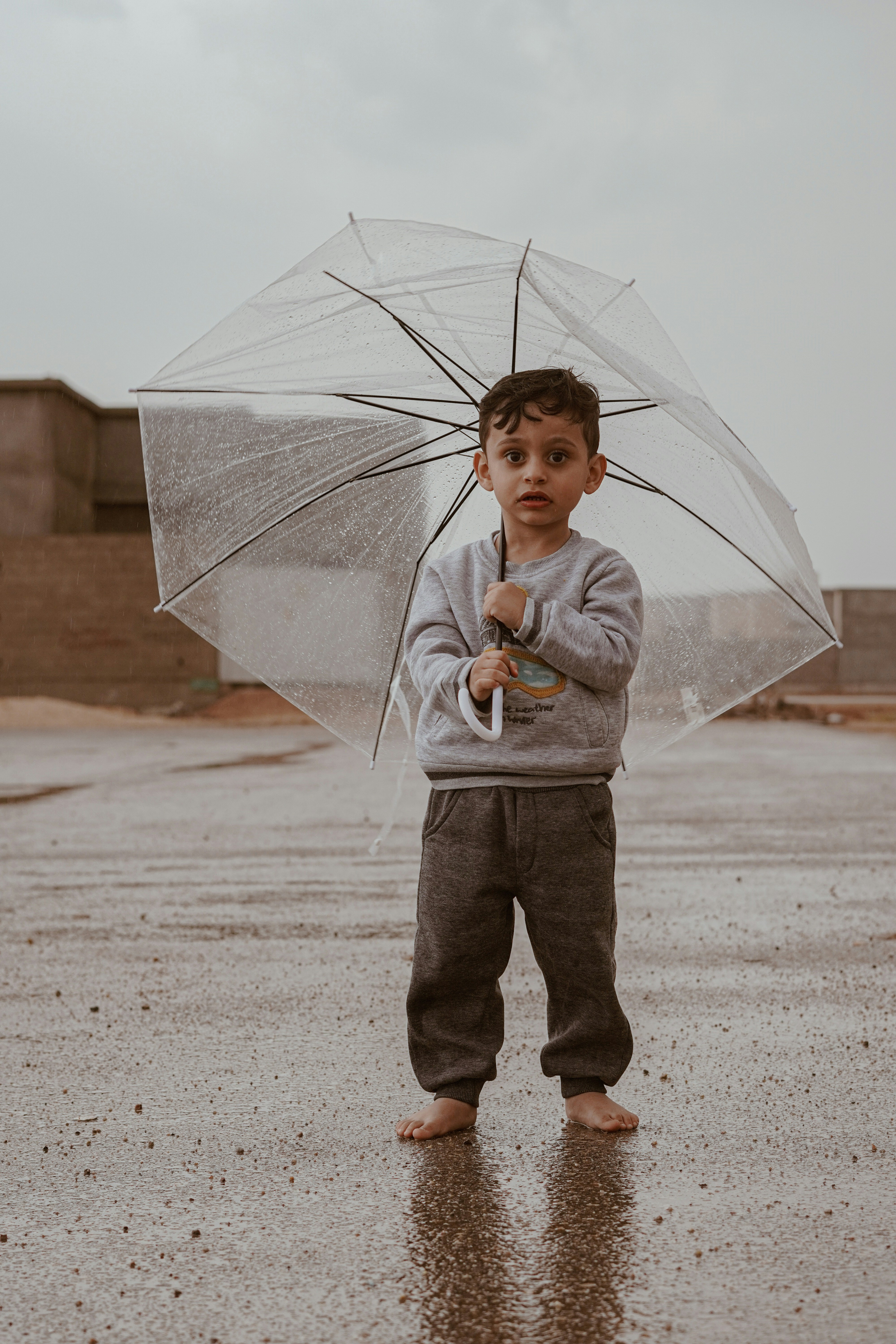 A little boy standing in the rain holding an umbrella
