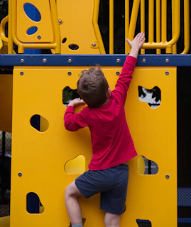 A young boy climbing up a yellow playground structure