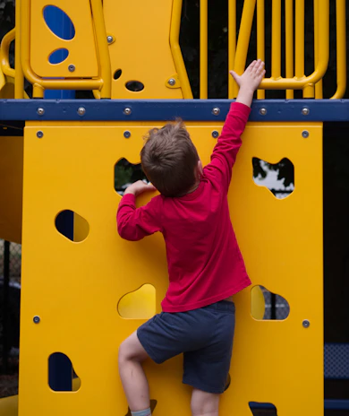 A young boy climbing up a yellow playground structure