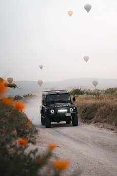 A jeep driving down a dirt road surrounded by hot air balloons