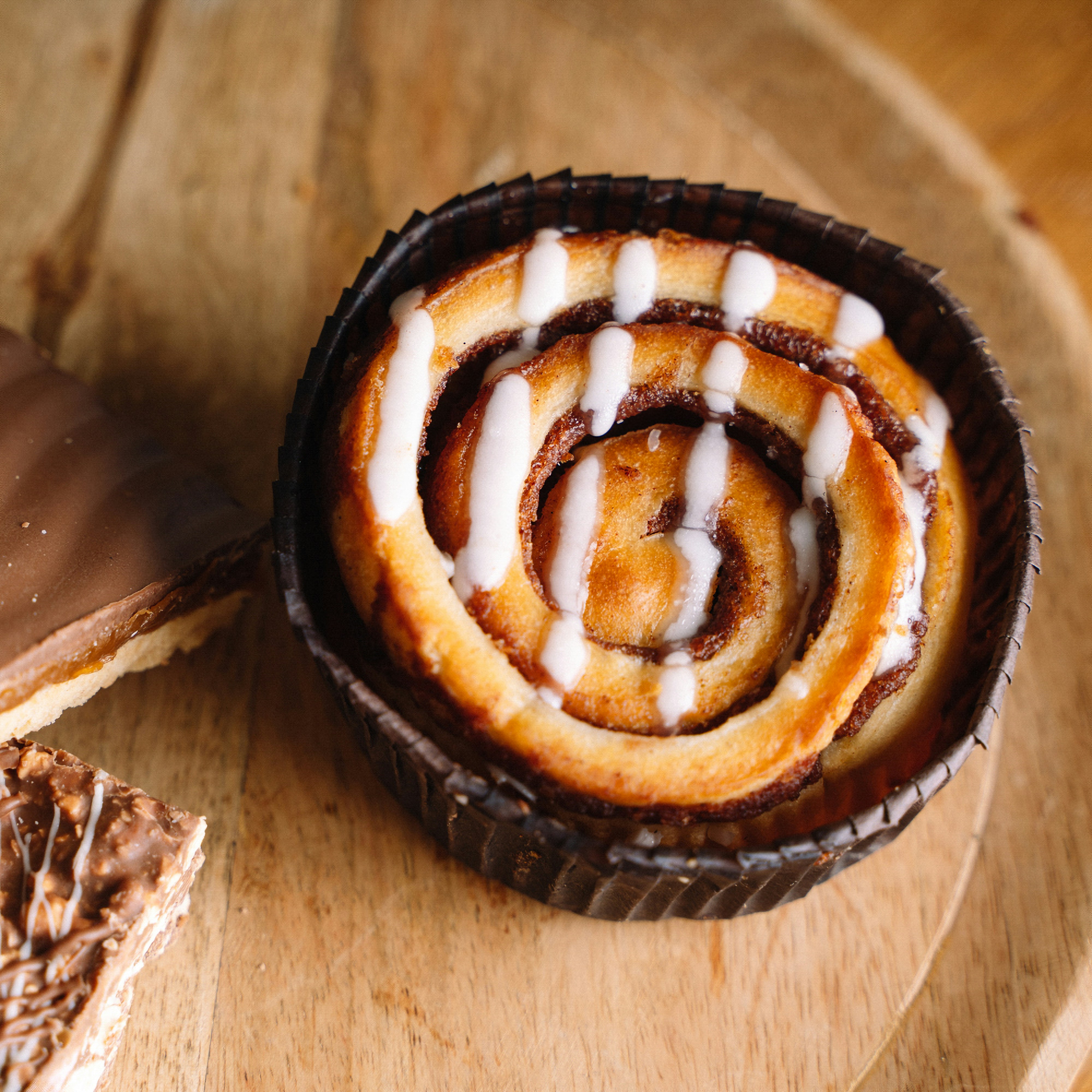A wooden plate topped with a pastry next to a slice of cake