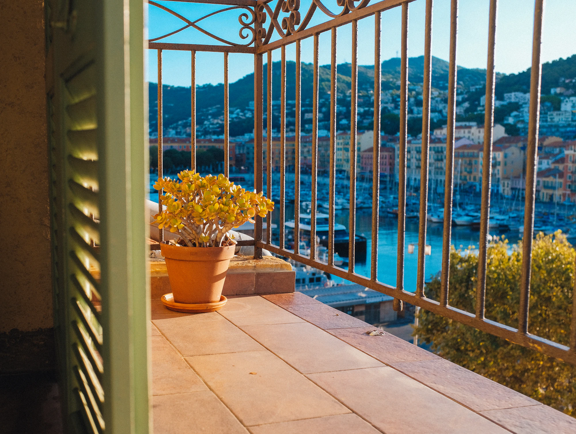 Balcon aux volets verts ouvrant sur un port méditerranéen