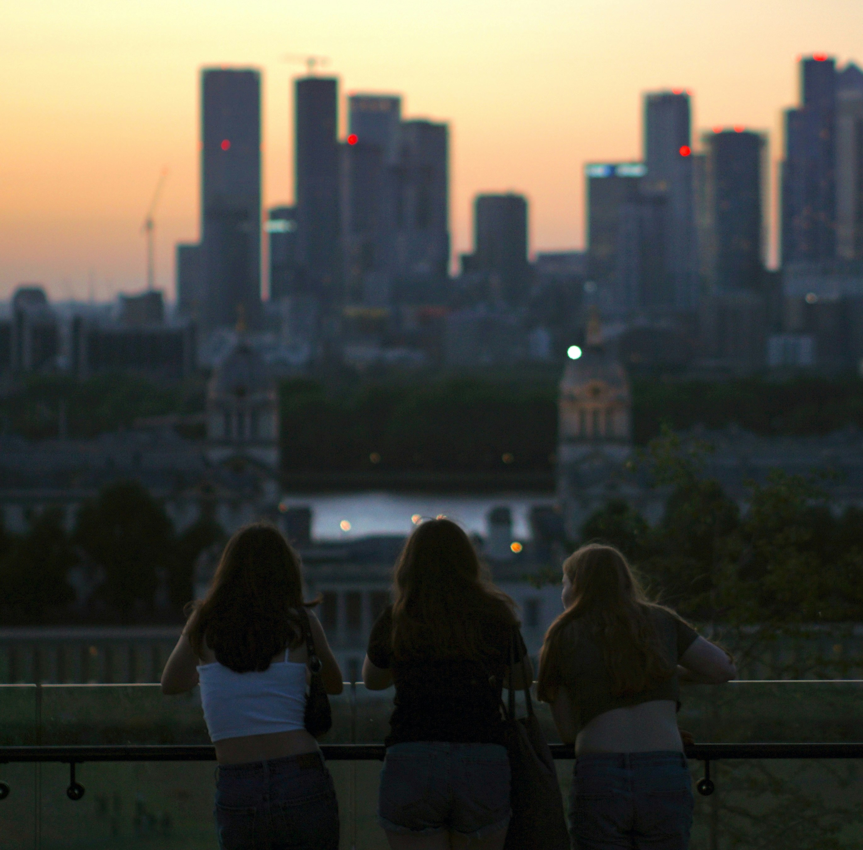 Three girls are sitting on a bench looking at the city