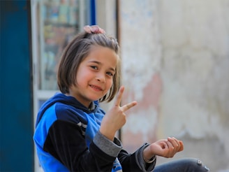 A little girl sitting on the ground making a peace sign