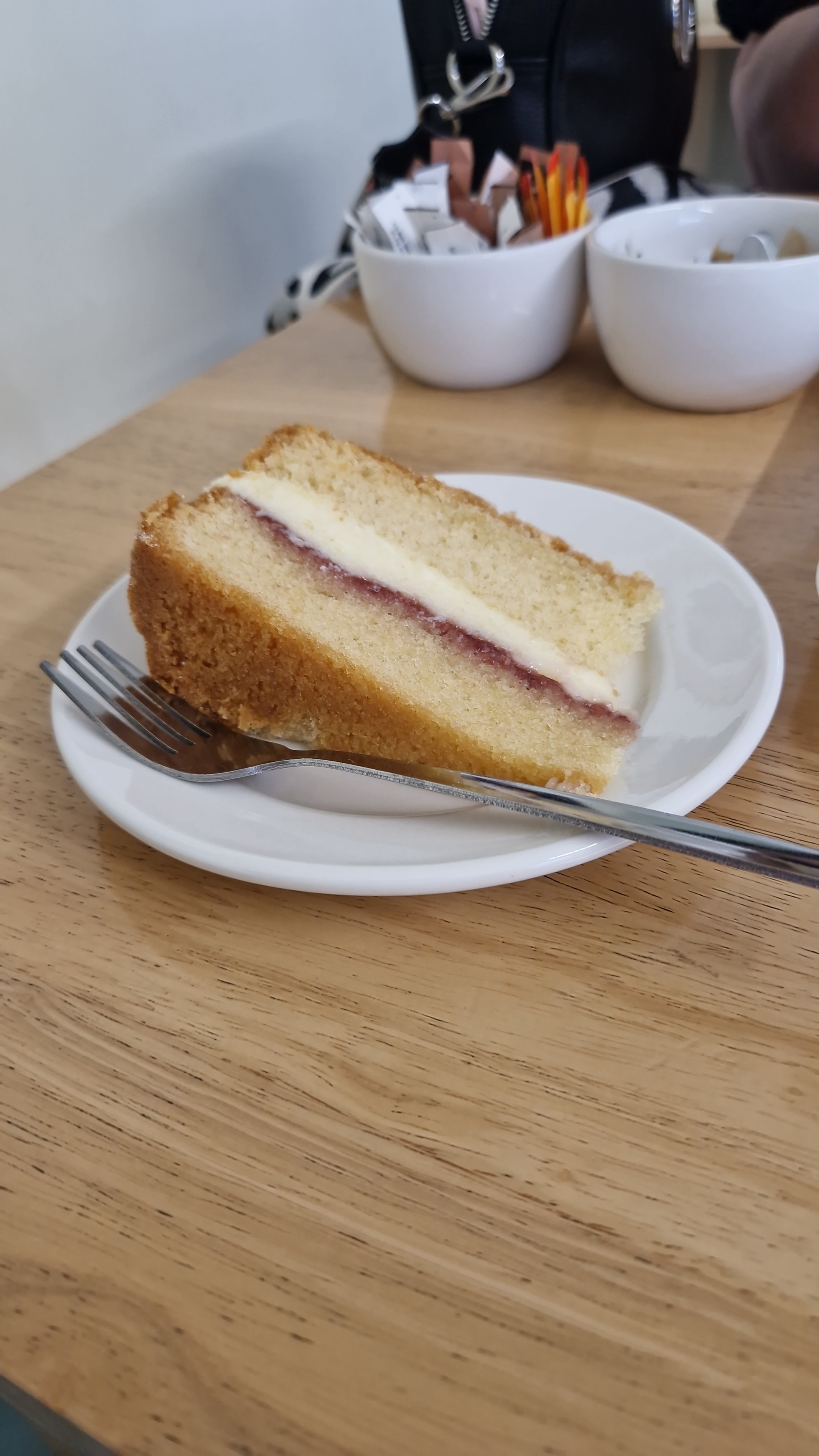 Slice of Victoria sponge cake with cream and jam filling on a white plate, soft natural light