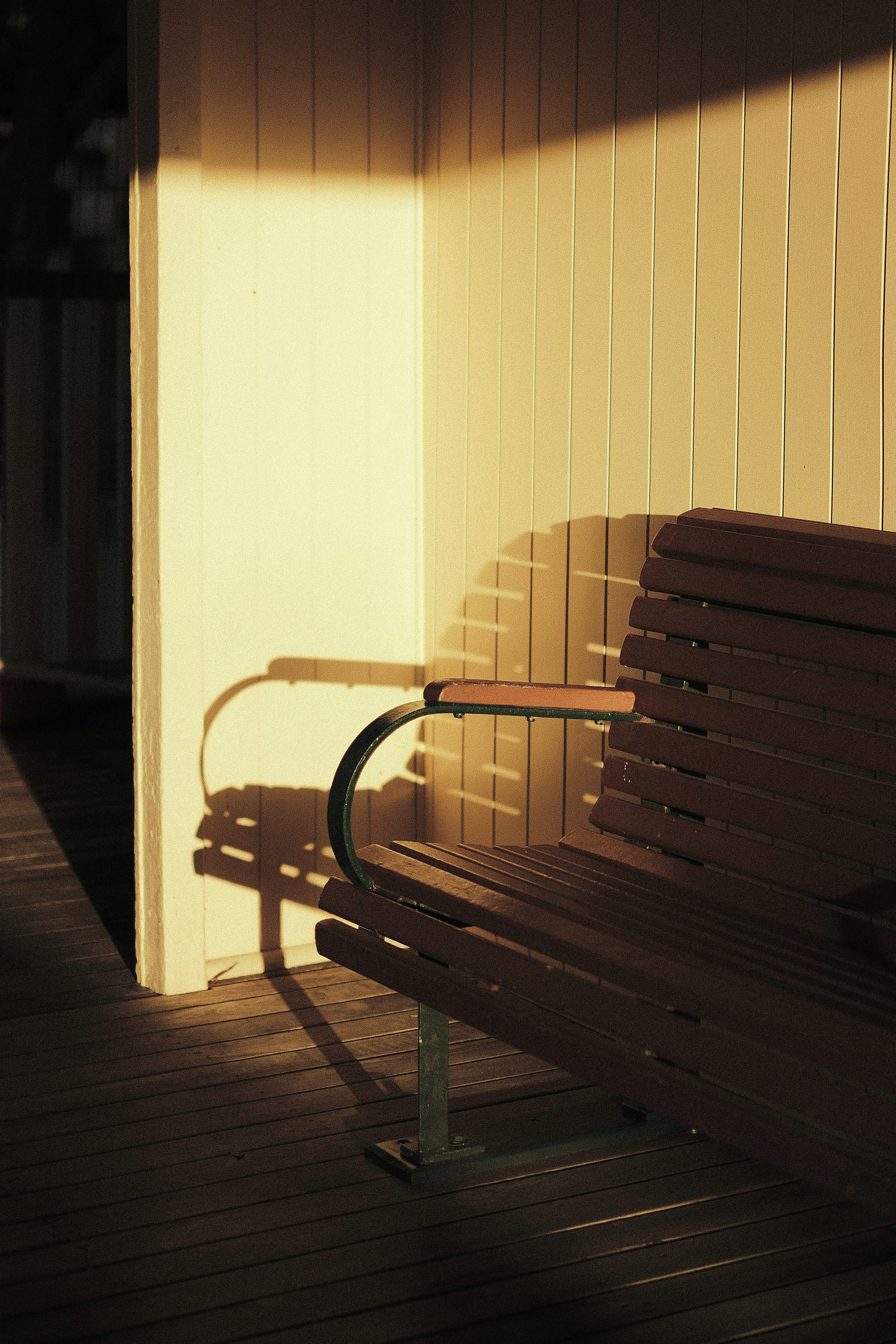 Sunlight casts elongated shadows of a bench on a wooden deck, highlighting the interplay of light and texture in a serene setting.