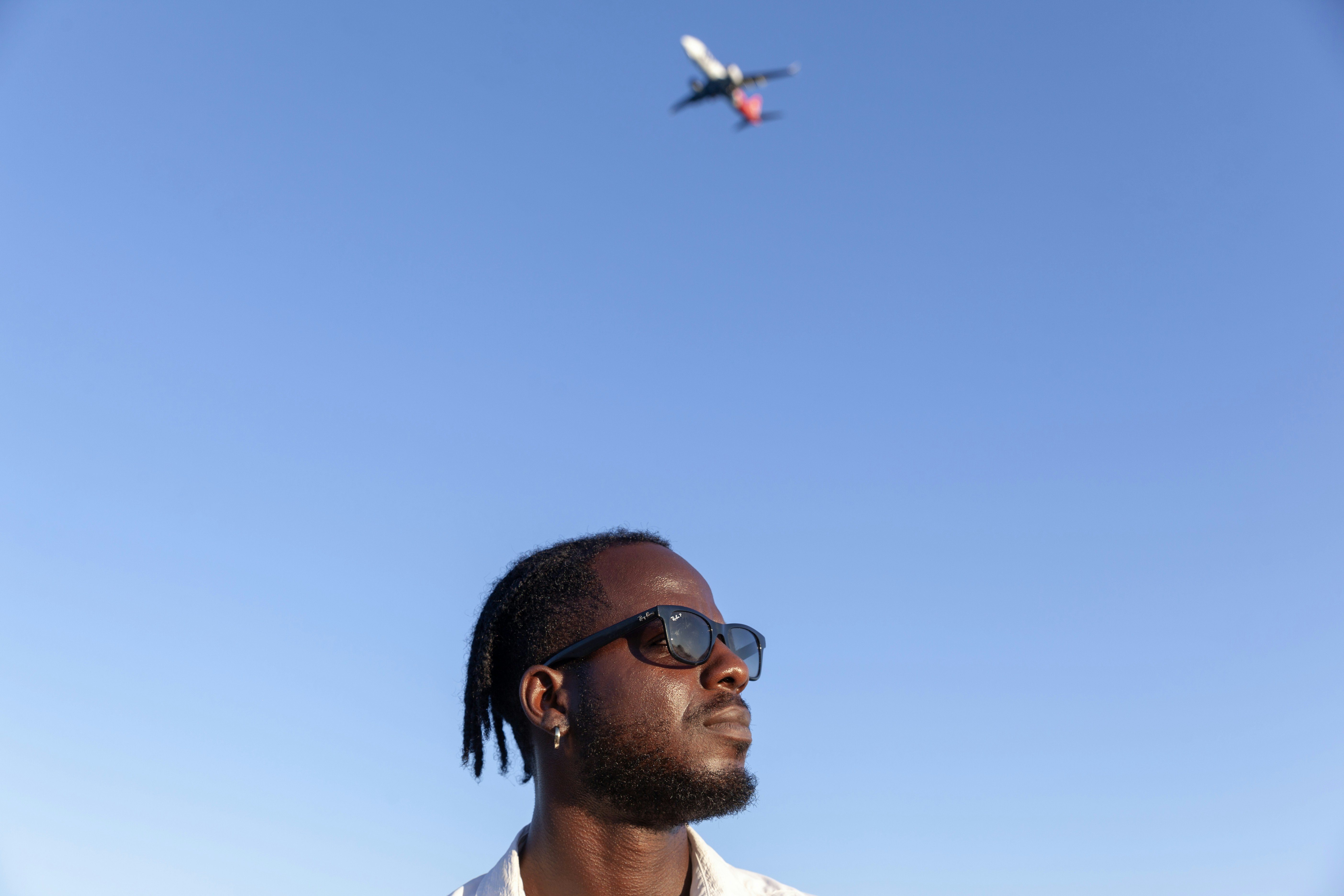 A man wearing sunglasses looking up at a plane in the sky