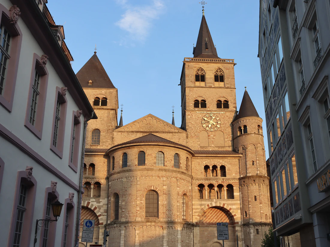 Westbau des Trierer Doms mit Turmuhr in goldener Abendsonne, links eine Altstadtfassade