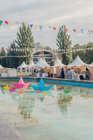 A group of people standing next to a pool filled with paper boats