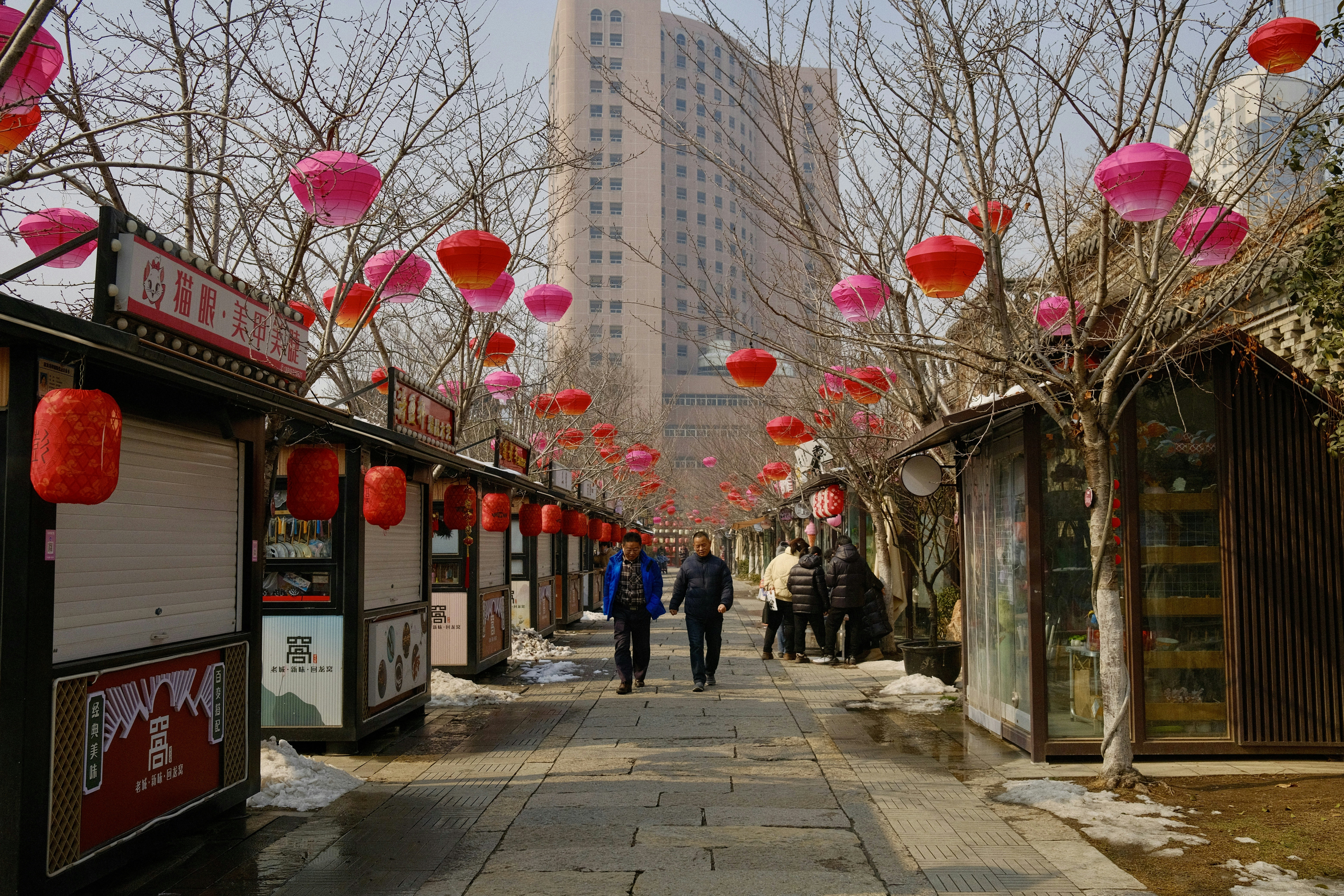 A group of people walking down a street next to a tall building