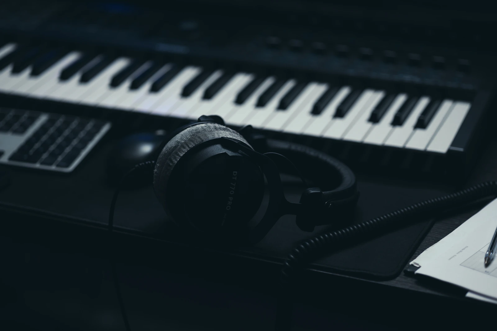 A synthesizer keyboard with studio headphones and a microphone on a dark desk