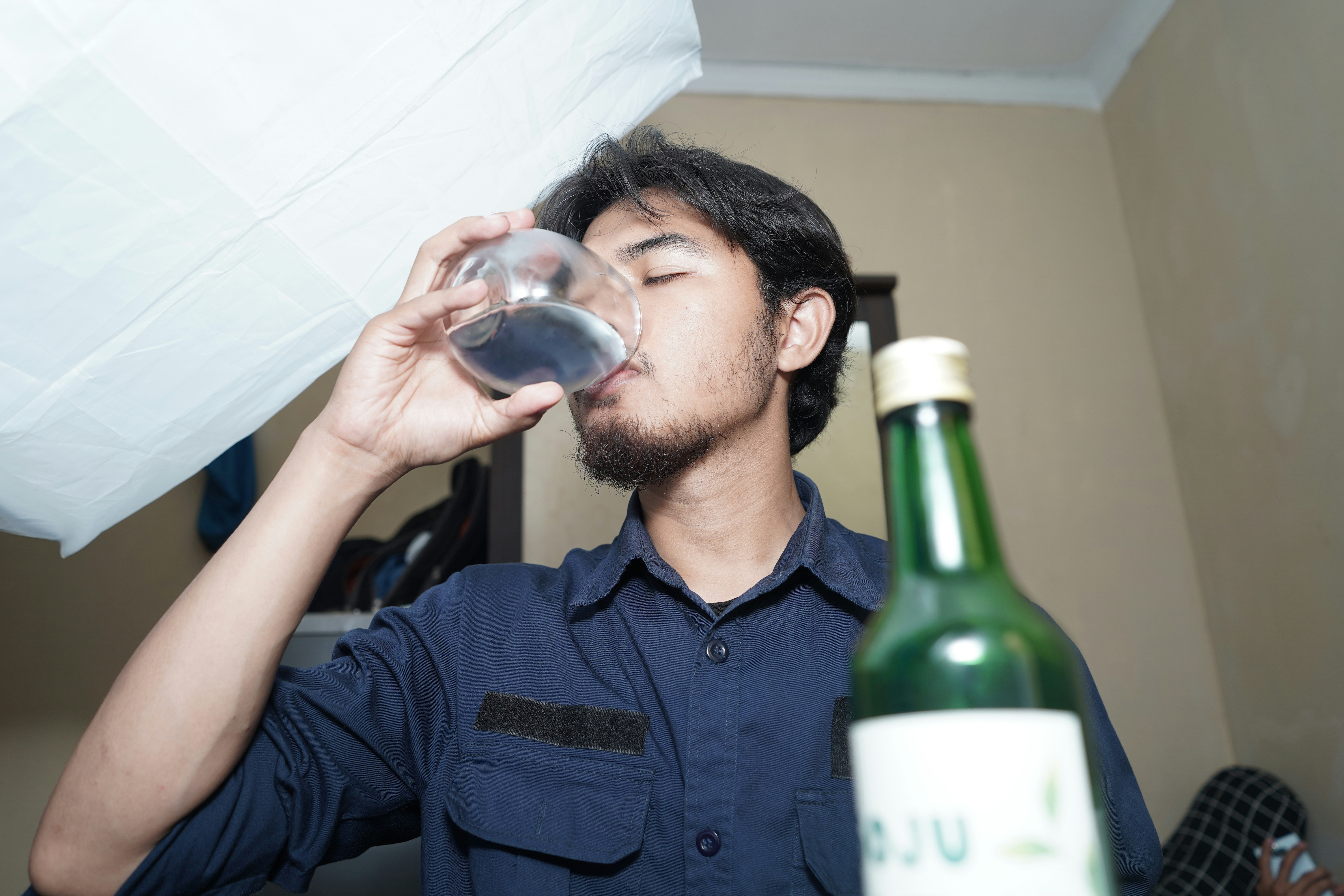 A man drinking from a wine glass next to a bottle