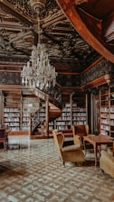 A library with a chandelier, couches, and tables