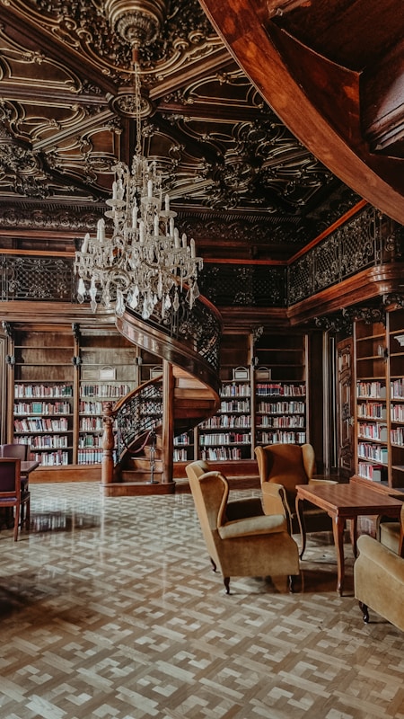 A library with a chandelier, couches, and tables