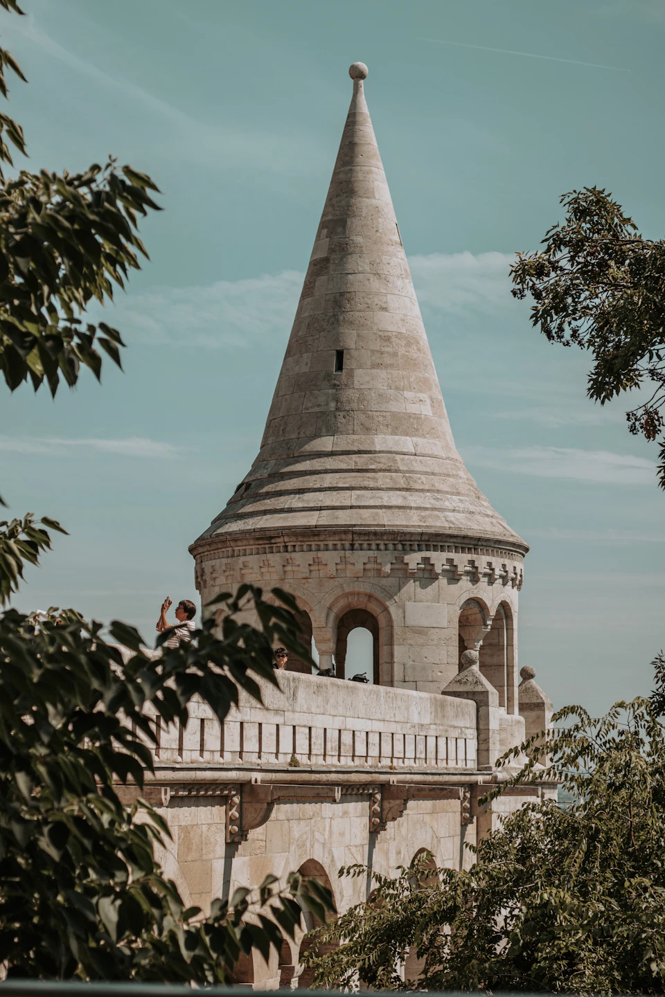 Stone tower with pointed roof stands tall against clear blue sky on hilltop