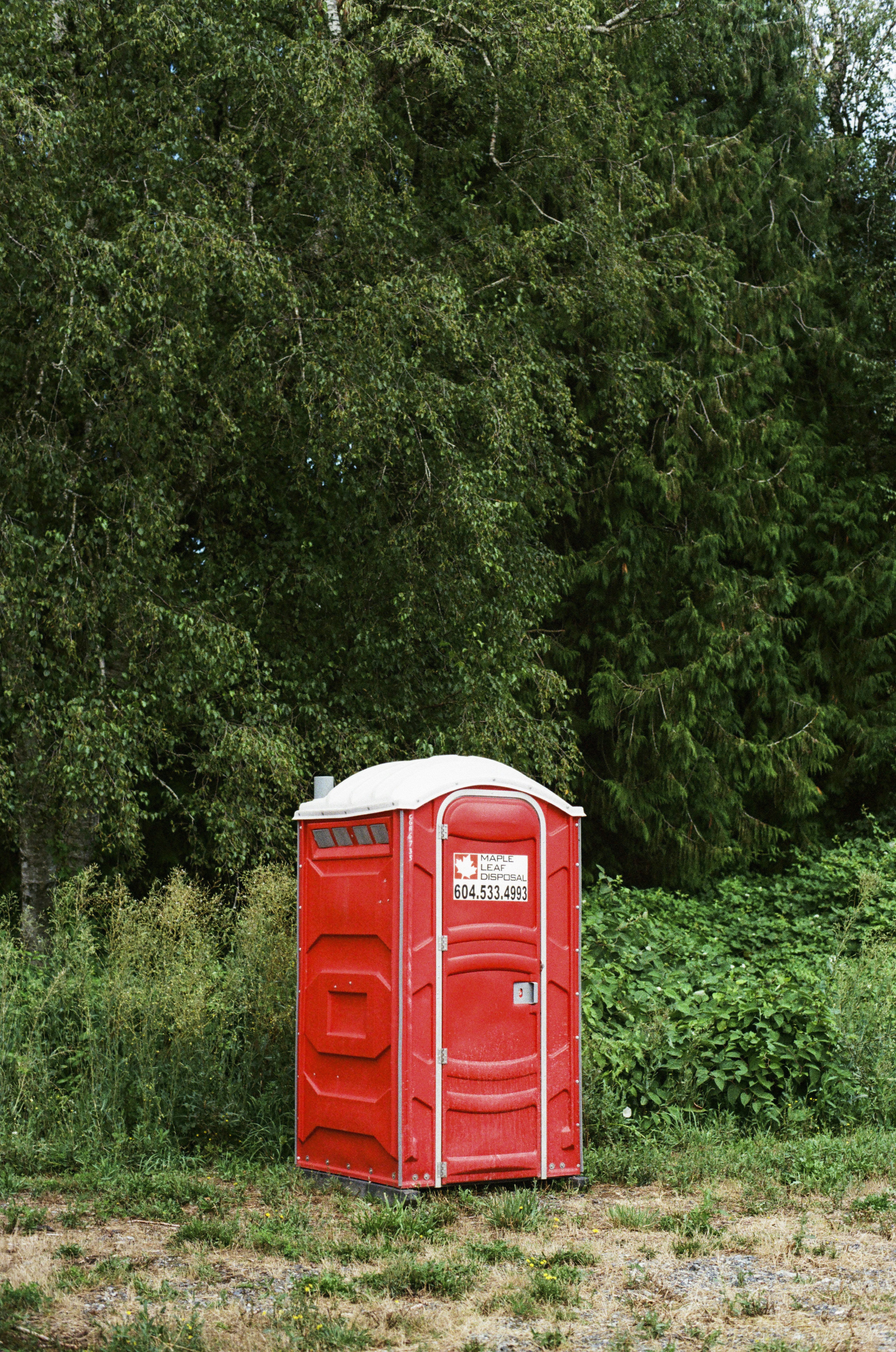 A red outhouse sitting in the middle of a field