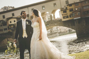A bride and groom standing in front of a river