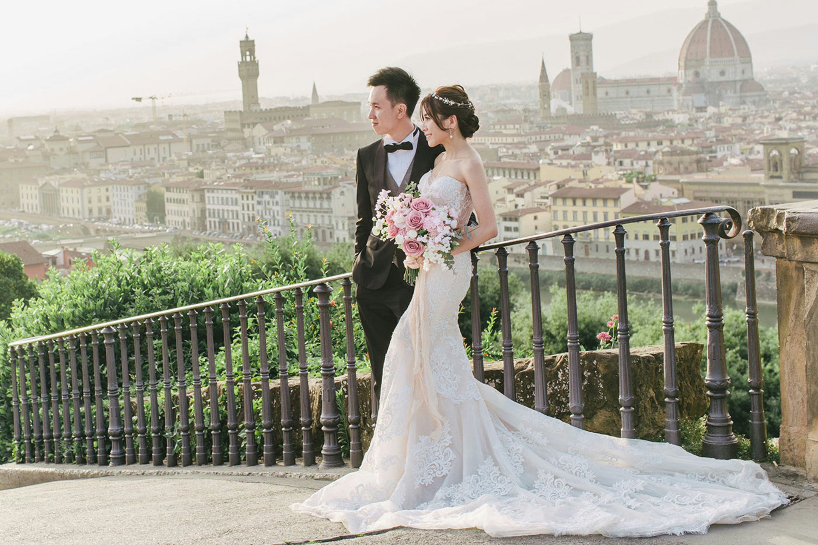 A bride and groom standing on a balcony overlooking a city