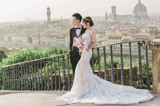 A bride and groom standing on a balcony overlooking a city