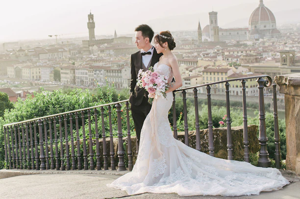 A bride and groom standing on a balcony overlooking a city