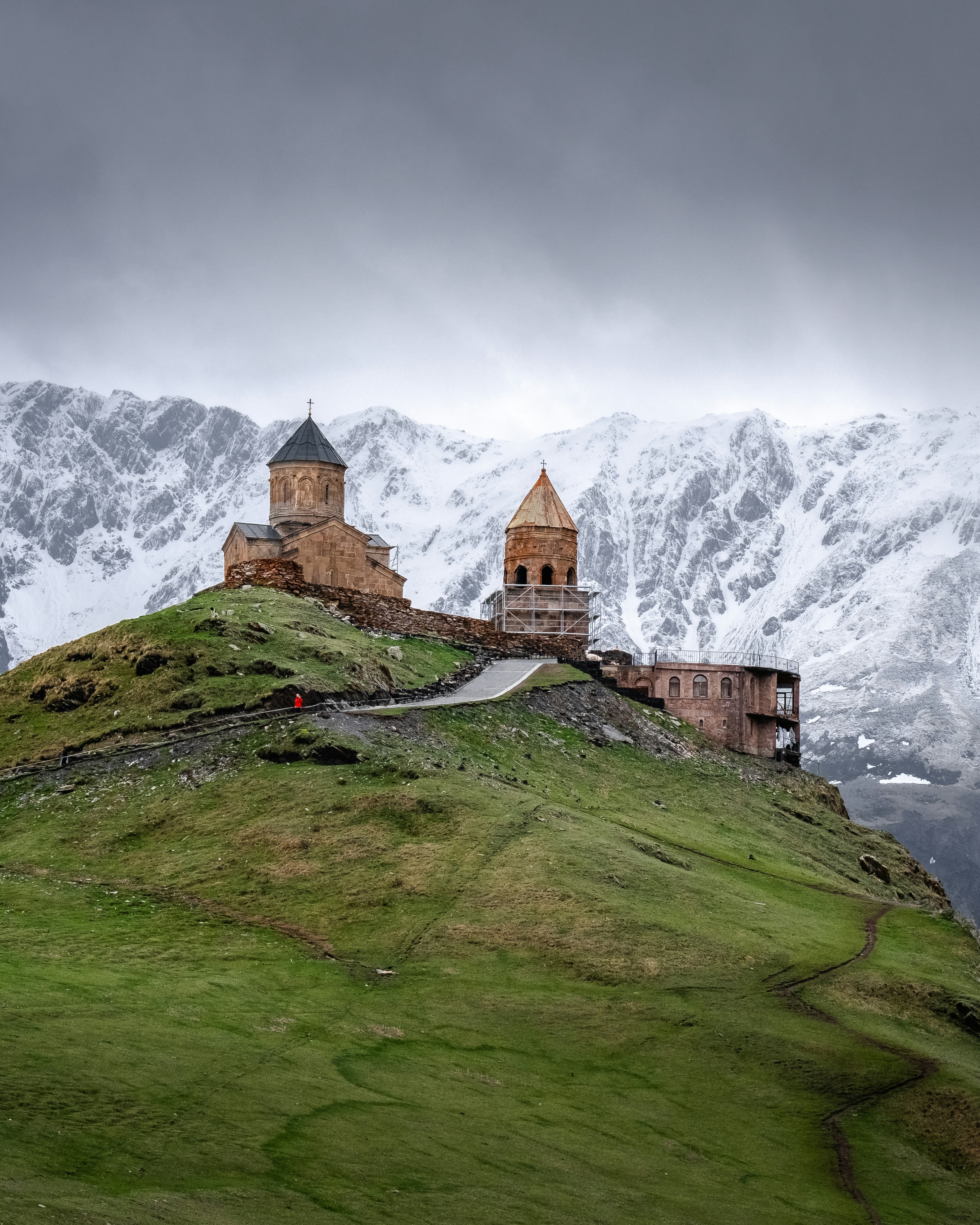 A castle on top of a green hill with snow covered mountains in the background