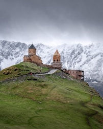A castle on top of a green hill with snow covered mountains in the background
