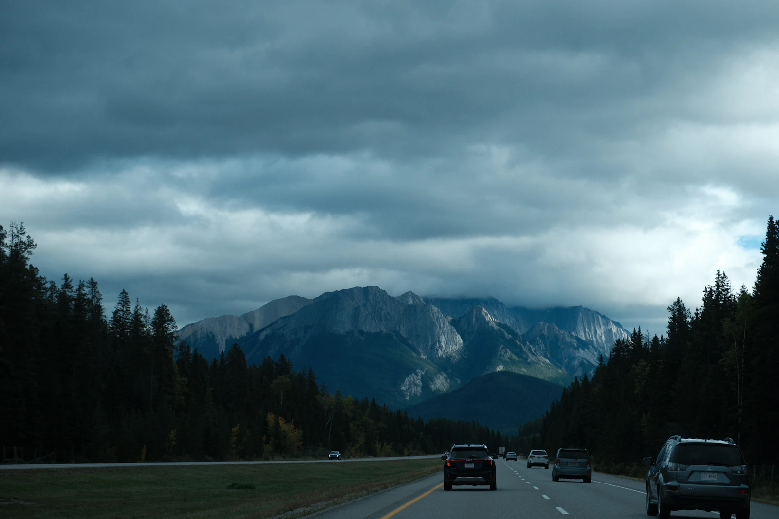 Cars travel beneath cloud and mountains in Banff