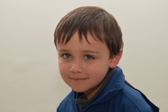 A young boy wearing a blue jacket and smiling