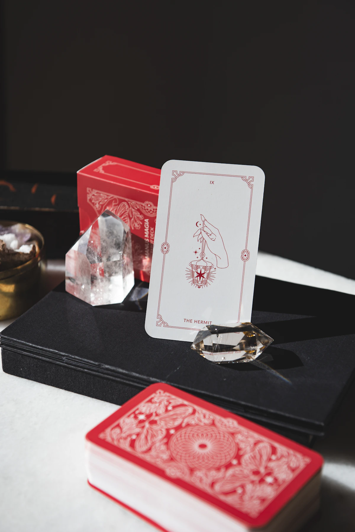 A tarot card standing on a dark surface next to its boxed deck and crystals